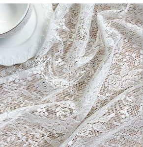 Close-up of white floral lace fabric with delicate embroidery and scalloped edges