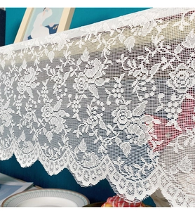 Detail of white crochet lace table runner with intricate rose patterns and wavy edges