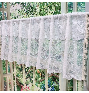 Close-up of white floral lace curtain with fringe tassels and semi-transparent texture
