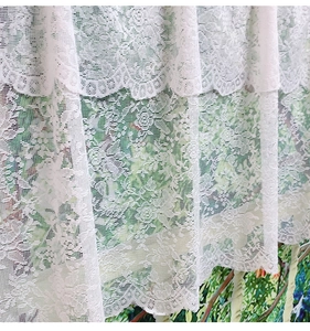 Macro detail of white lace kitchen curtain showing floral embroidery and fringe edges