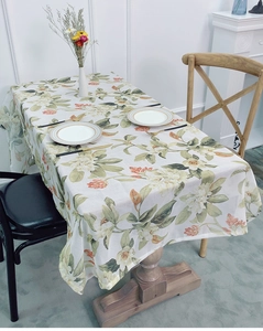 Detail of floral linen tablecloth with white gardenias and green leaves on a wooden table