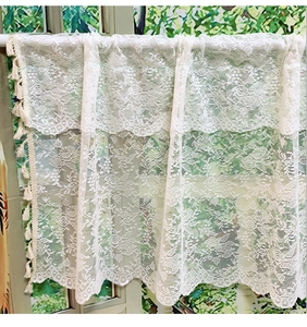 Detail of white French lace cafe curtain featuring crochet floral patterns and fringe pom poms