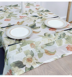Detail of floral linen tablecloth featuring white and orange flowers on a wooden dining table