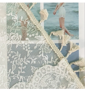 Detailed view of white lace curtain with floral embroidery and bohemian tassel fringe