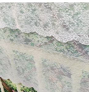 Detail of white lace kitchen curtain with floral hollow pattern and scalloped edges