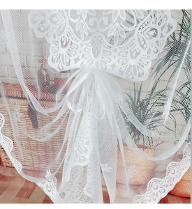 Détail du rideau en dentelle blanche avec broderie florale et nœud en ruban satiné