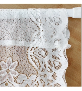 Détail du rideau en dentelle blanche avec motifs floraux et bords festonnés sur tringle