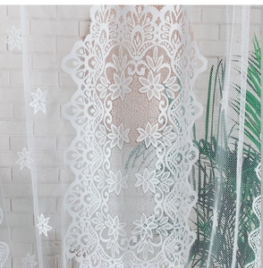 Détail du rideau en dentelle blanche avec motifs floraux et bordure en marguerite