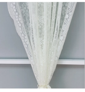 Detail der weißen Spitzengardine mit Blumenmuster und feinem Perlen-Raffhalter-Detail