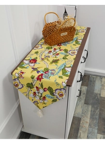 Detail of yellow cotton table runner with floral bird prints and white tassels