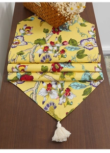 Detail of yellow floral table runner featuring botanical patterns and white cotton tassels