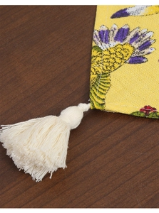 Detail of yellow cotton linen table runner featuring floral prints and cream tassels