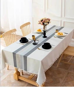 Detail of Nordic striped linen tablecloth with white decorative tassel edges on a wooden table