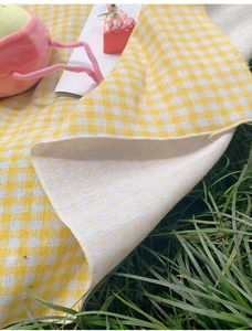 Detail view of yellow plaid picnic mat fabric texture on green grass outdoors