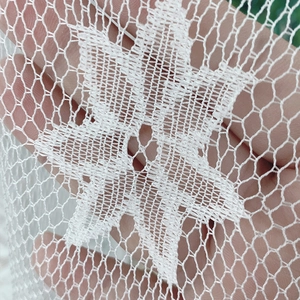 Rideau en dentelle blanche avec motifs d'étoiles montrant la transparence avec une main