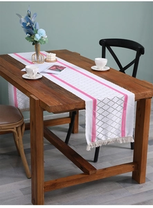 Detail of Nordic lace table runner with pink stripes and tassels on a wood table