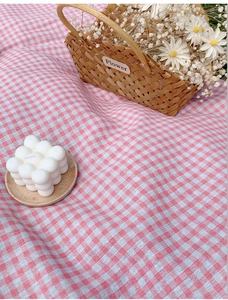 Detail of pink and white checkered picnic mat fabric with woven flower basket on grass