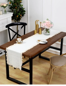 Détail de la texture du chemin de table en lin beige avec franges sur table en bois