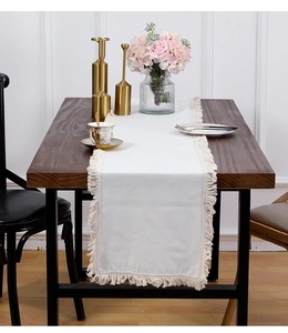 Détail de la texture du chemin de table en coton beige avec franges sur table en bois