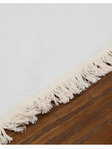 Détail de chemin de table en coton lin crème avec franges sur fond bois foncé