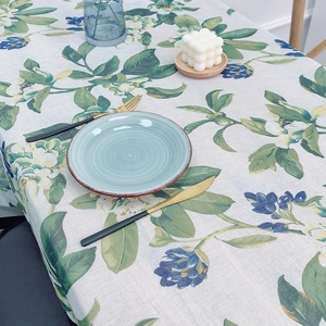 Floral linen tablecloth with green leaves and white flowers in a rustic dining setting