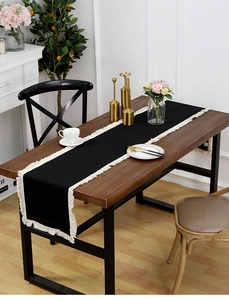 Détail du chemin de table noir en coton et lin avec des glands blancs sur bois