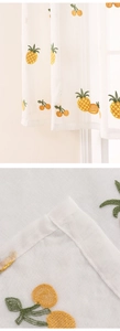 Close-up of white lace curtain with embroidered yellow pineapples and orange cherries