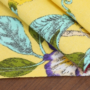 Floral table runner with blue leaves on yellow cotton-linen fabric over wood surface