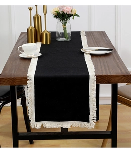 Détail d'un chemin de table noir avec glands blancs sur une table à manger en bois