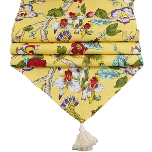 Floral table runner with yellow orchid print and white tassels on a minimalist background