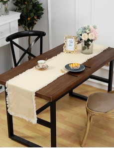 Détail du chemin de table en lin blanc cassé avec franges élégantes sur table en bois
