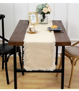 Détail d'un chemin de table en lin beige avec des bordures à franges sur table en bois