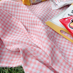 Portable red and white checkered outdoor picnic mat with tassels on green grass