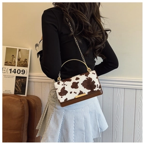Detail of cow print crossbody bag with gold handle and chain strap on a leather sofa