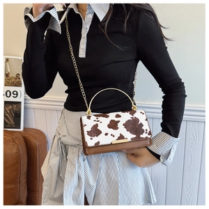 Detail of cow print handbag with gold circular metal handle and chain strap