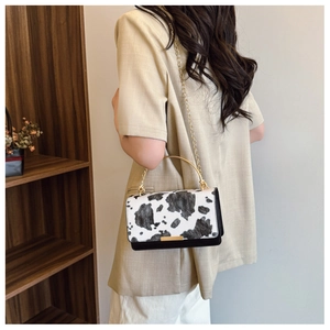 Detail of cow print handbag with golden metal handle and matching chain shoulder strap