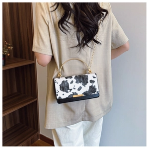 Cow print crossbody bag detail showing gold handle and chain strap on a model