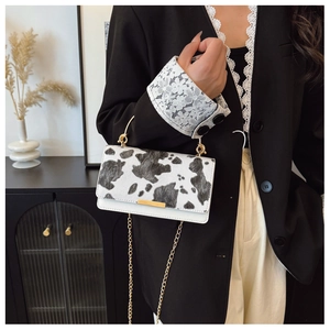Detail of cow print mini bag featuring gold metal handle and chain strap on black blazer