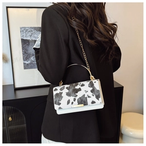 Chic cow print faux fur crossbody bag featuring a golden metal handle and chain strap detail