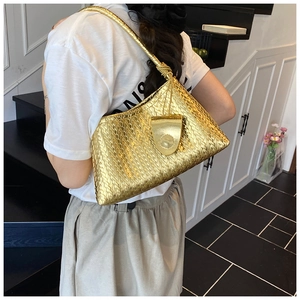 Close-up of golden woven shoulder bag with knotted strap detail on a female model