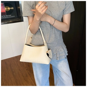 Detailed close-up of woven cream underarm bag with matching circular leather charm