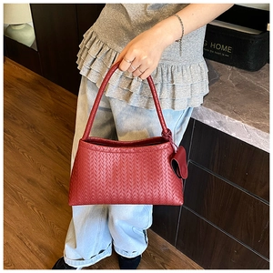 Close-up of a red woven leather bucket bag with a heart charm worn by a model