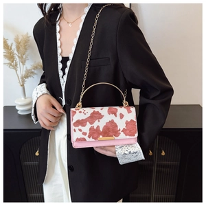 Fashionable cow print handbag with pink leather base and gold metal handle shown on model