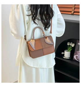 Detail view of a brown color-block handbag with a plaid silk scarf wrapped around the handle