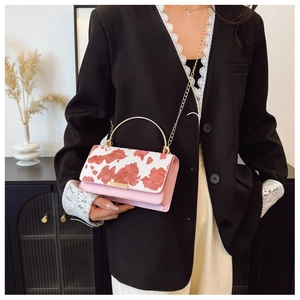 Pink and white cow print handbag with gold arched handle and chain strap on model