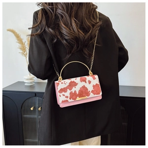 Detail of pink cow print handbag with golden metal handle and chain on black blazer