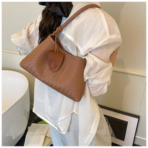 Close-up of caramel woven leather shoulder bag with circular buckle on model