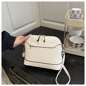 Detail of white woven shell bag showing dual gold zippers and sleek texture