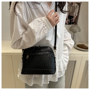 Detail view of black woven shell crossbody bag with gold hardware worn by a model