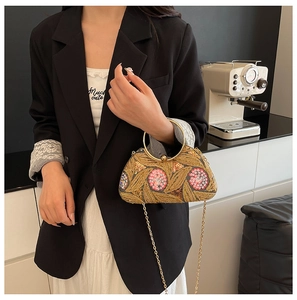 Detailed embroidery on a gold sequin evening clutch bag held by a model in a suit